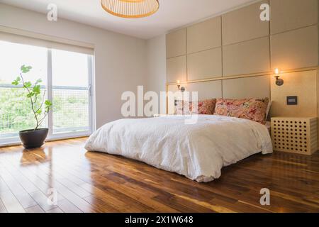 King-Size-Bett mit weißer Bettdecke im Schlafzimmer mit amerikanischem Walnussholzfußboden im Obergeschoss im modernen Cube-Stil Haus, Quebec Stockfoto