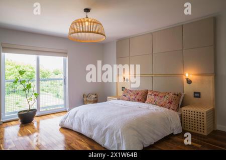 King-Size-Bett mit weißer Bettdecke im Schlafzimmer mit amerikanischem Walnussholzfußboden im Obergeschoss im modernen Cube-Stil Haus, Quebec Stockfoto