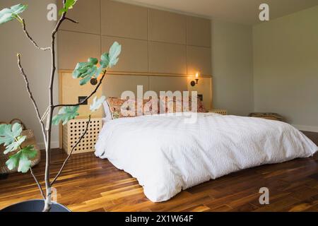 King-Size-Bett mit weißer Bettdecke im Schlafzimmer mit amerikanischem Walnussholzfußboden im Obergeschoss im modernen Cube-Stil Haus, Quebec Stockfoto