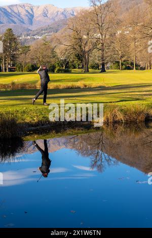 Männlicher Golfer reflektierte sich in einem Wasserteich und schlug den Golfball auf dem Fairway auf dem Golfplatz mit Mountain an einem sonnigen Tag in der Schweiz. | HERR:ja Stockfoto