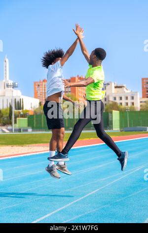 Vertikales Foto von zwei afroamerikanischen jungen Freunden, die auf einer Laufstrecke springen und feiern und Hände halten Stockfoto