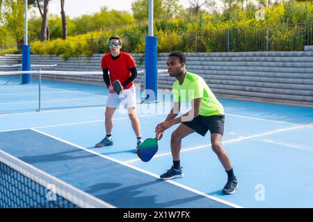 Foto in voller Länge von einem multirassischen Team von Pickleball-Spielern auf einem Outdoor-Platz an einem sonnigen Tag Stockfoto