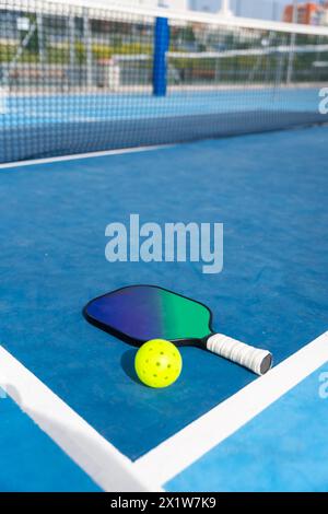 Vertikales Foto mit Kopierraum eines Schlägers und eines gelben Pickleball-Balls auf einem Platz Stockfoto