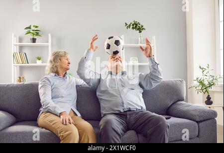 Senior Family Pärchen Sitzen Auf Dem Sofa, Ehemann Spielt Zu Hause Mit Fußball Stockfoto