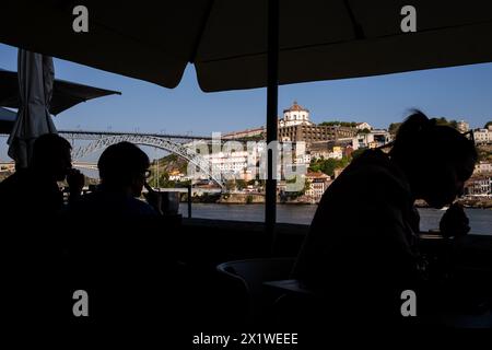 Silhouetten von Touristen auf der Terrasse eines Bar-Restaurants mit Blick auf den Fluss Douro, die Dom-Luis-Brücke und die Igreja do Mosteiro de Sa Stockfoto