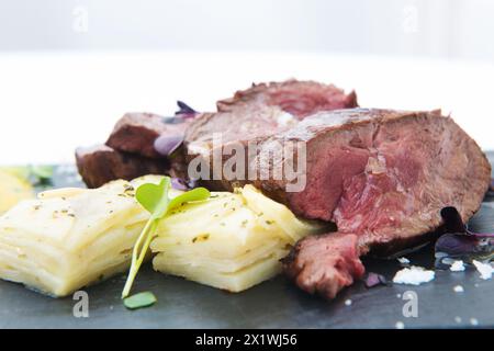 Geschnittenes Roastbeef mit Kartoffeln und Kräutern auf einem schwarzen Teller Stockfoto