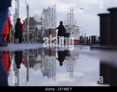 Hamburg, Deutschland. April 2024. Die Elbphilharmonie spiegelt sich in einer Pfütze an den Landungsbrücken im Hafen wider. Quelle: Marcus Brandt/dpa/Alamy Live News Stockfoto