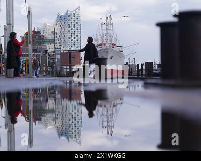 Hamburg, Deutschland. April 2024. Die Elbphilharmonie spiegelt sich in einer Pfütze an den Landungsbrücken im Hafen wider. Quelle: Marcus Brandt/dpa/Alamy Live News Stockfoto