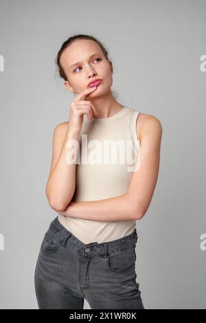 Junge Frau posiert tief in Gedanken auf grauem Hintergrund Stockfoto