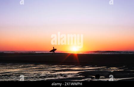 Surfer auf dem Rückweg vom Meer bei Sonnenuntergang Stockfoto