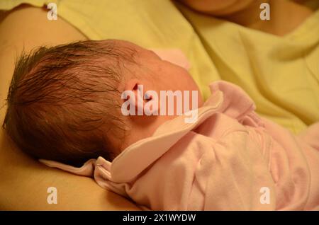 Frau in gelber Kleidung, mit ihrem neugeborenen Baby auf dem Schoß, in rosa Kleidung, Ohren und Haare zeigen. Eine Mutter und eine Tochter werden geboren. Stockfoto