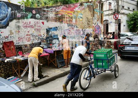 Straßenverkäufer in Lapa in der Nähe der Selaron Steps, mit farbenfroher Straßenkunst dahinter. Stockfoto