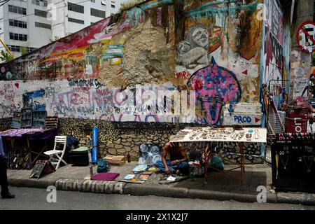 Straßenverkäufer in Lapa in der Nähe der Selaron Steps, mit farbenfroher Straßenkunst dahinter. Stockfoto