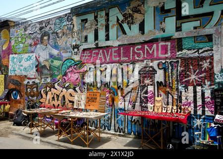 Straßenverkäufer in Lapa in der Nähe der Selaron Steps, mit farbenfroher Straßenkunst dahinter. Stockfoto