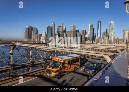 Gelber Schulbus auf der Brooklyn Bridge über den East River mit Lower Manhattan Wolkenkratzern dahinter. New York Stockfoto