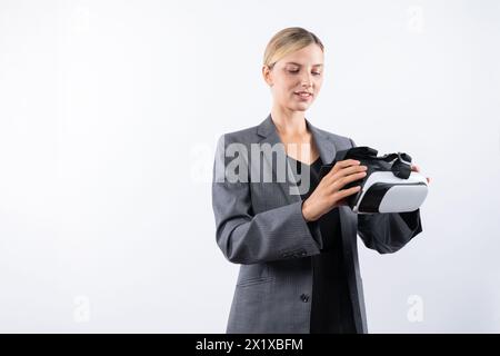 Kaukasische Geschäftsfrau hält VR-Glas, während sie auf weißem Hintergrund steht. Professioneller Projektmanager, der beim Tragen eine visuelle Reality-Brille sieht Stockfoto