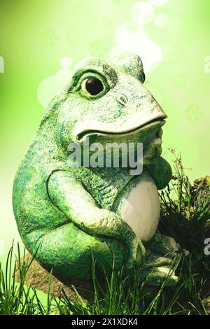 Froschdekoration Hintergrund. Eine dekorative alte verwitterte keramische Froschfigur, die auf einem Stein über abstraktem hellgrünem Sommerhintergrund sitzt. Stockfoto