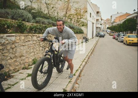 40 Jahre alter junger Mann, der E-Mountainbike die Straße hochschiebt. Aktiver Lebensstil. Sport. Abenteuerfahrt mit dem Fahrrad. Mit dem el-Bike Stockfoto
