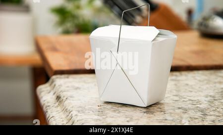 Aus nächster Nähe eine weiße chinesische Take-Out-Box mit dem ikonischen Metallgriff auf einer Küchenplatte aus Granit Stockfoto