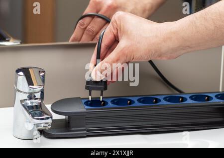 Nahaufnahme eines Mannes, der den Stecker A in eine Steckdose im Badezimmer steckt Stockfoto