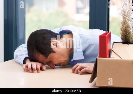 Ein trauriger gefeuerter Manager, der weint und ihre Sachen auf eine Kiste im Büro packt Stockfoto