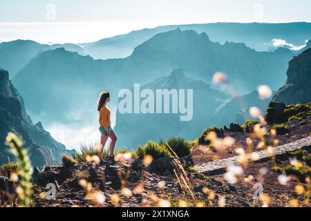 Beschreibung: Weibliche Toruist steht am windigen Rand eines tiefen, wolkenbedeckten Tals und genießt den atemberaubenden Panoramablick auf den vulkanischen Berg Stockfoto