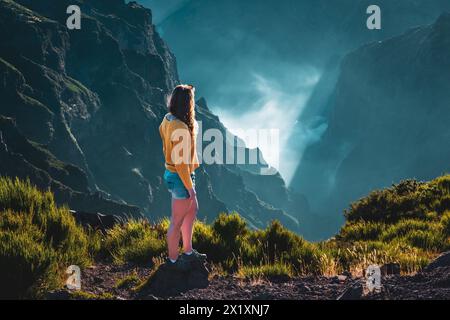 Beschreibung: Sportlicher Frauentoursit überblickt die atemberaubenden Tiefen eines wolkenbedeckten Tals und genießt den Blick auf den vulkanischen Berg ap Stockfoto