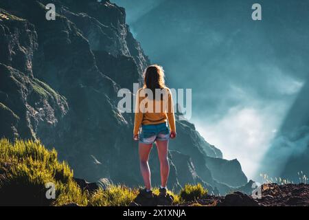 Beschreibung: Sportlicher Frauentoursit überblickt die atemberaubenden Tiefen eines wolkenbedeckten Tals und genießt den Blick auf die vulkanische Berglandschaft. Stockfoto