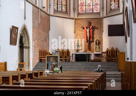 Ein einsamer Mann kniet im Gebet in der St. Adalberts Kirche in Breslau, Polen, gegenüber dem Altar mit Kruzifix und lebendigen Buntglasfenstern. Kosciol Schalter Stockfoto