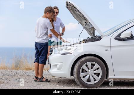 Eine junge Frau mit ihrem Sohn, die am Pannenwagen steht und Probleme mit dem Fahrzeug hat Stockfoto