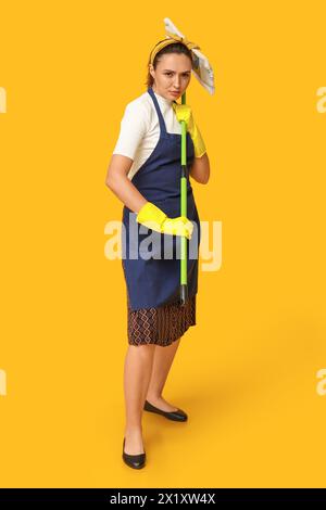 Porträt einer fokussierten jungen Hausfrau in Schürze mit Mopp auf gelbem Hintergrund Stockfoto