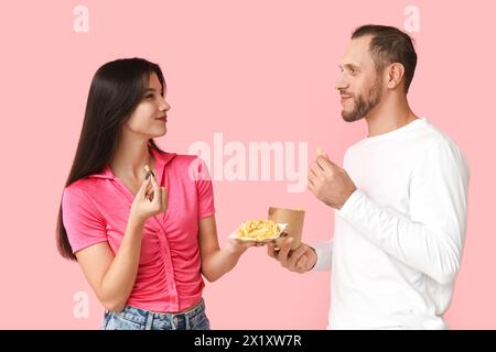 Schönes junges Paar mit Pommes frites auf rosa Hintergrund Stockfoto