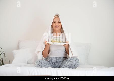 Reife Frau mit Handtuch, die im Schlafzimmer Dampf einatmet Stockfoto