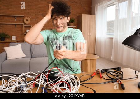 Ein junger Mann mit Verbrennungsgesicht und Drähten auf dem Tisch zu Hause Stockfoto