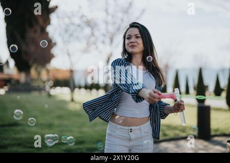 Junge Frau, die fröhlich mit Blasen in einer sonnigen Parklandschaft spielt Stockfoto