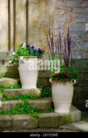 Treppe mit zwei großen Tontöpfen mit blühenden Pflanzen im Sommer vor einer strukturierten Steinmauer, die zu einer mittelalterlichen Klosterkirche gehört. Stockfoto