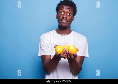 afroamerikanischer Mann, der Zitronen trägt und in die Kamera schaut. Schwarzer Mann hält und zeigt gelbe Zitrusfrüchte für Vitamine, Ernährung und gesunden Lebensstil. Stockfoto