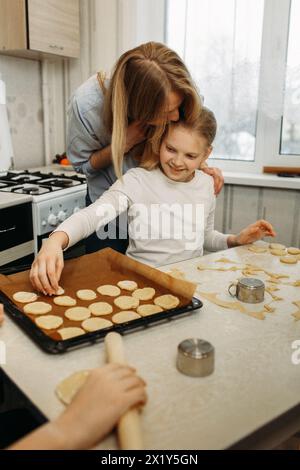 Eine Frau hilft einem jungen Mädchen beim Keksbacken in der Küche. Die Frau führt das Mädchen durch die Schritte der Keksherstellung, vom Mixin Stockfoto