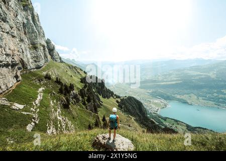 Beschreibung: Bergsteiger steht auf einem Felsen neben dem Wanderweg und genießt den Blick auf den Walensee und die Walenstadt. Schnürliweg, Walensee, St. Ga Stockfoto