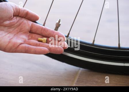 Nahaufnahme eines Radreifen-Ventiladapters auf der flachen Hand einer Person. Im Hintergrund eine Teilansicht eines Fahrradreifens mit Ventil. Stockfoto