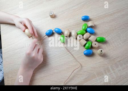 Kleines Kind, Kind, das farbige Holzperlen an einer Schnur reitet, Kinderfinger in Nahaufnahme, Konzept der Entwicklung der Feinmotorik, Tastsinn Stockfoto