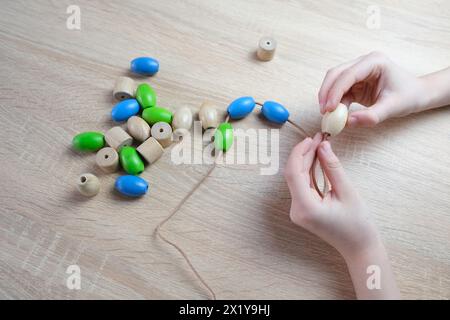 Kleines Kind, Kind, das farbige Holzperlen an einer Schnur reitet, Kinderfinger in Nahaufnahme, Konzept der Entwicklung der Feinmotorik, Tastsinn Stockfoto