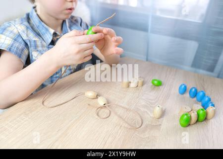 Kleines Kind, Kind, das farbige Holzperlen an einer Schnur reitet, Kinderfinger in Nahaufnahme, Konzept der Entwicklung der Feinmotorik, Tastsinn Stockfoto