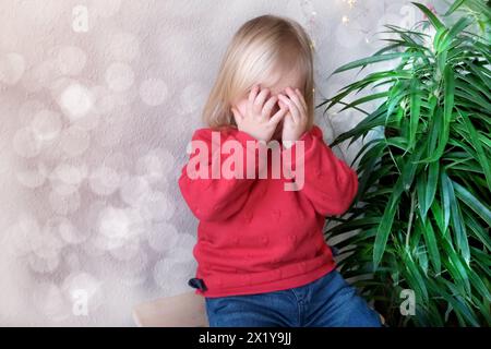 Kleines Kind, Baby, blondes Mädchen bedeckte ihr Gesicht mit ihren Handflächen vor Beleidigung, Weinen, Elternkonzept, Missbrauch, Bestrafung, die Launen der Kinder Stockfoto