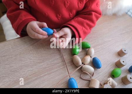 Kleinkind, Kleinkind, das farbige Holzperlen an einer Schnur anreiht, Kinderfinger in Nahaufnahme, Konzept der Entwicklung der Feinmotorik, Tastsinn Stockfoto