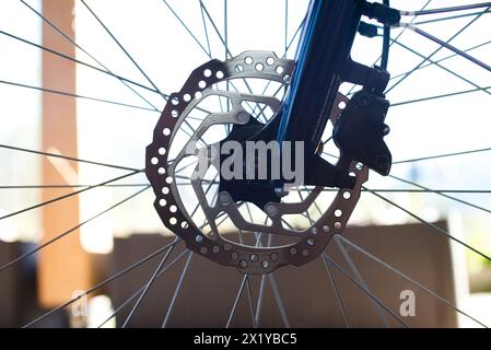 Nahaufnahme des Vorderrads eines E-Bikes mit einer Bremsscheibe aus Edelstahl, einem Bremssattel und einem Abschnitt der dunkelblauen Hochglanzgabel. Stockfoto