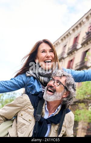 Älterer Mann Huckepack reife Frau, die Freizeit genießt, die europäische Stadt zu besuchen. Begeisterte Menschen. Stockfoto