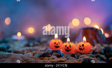 Halloween-Hintergrund, 3 Kerzen in Kürbisform im Vordergrund vor einem unscharfen Hintergrund mit gelben Lichtern Stockfoto