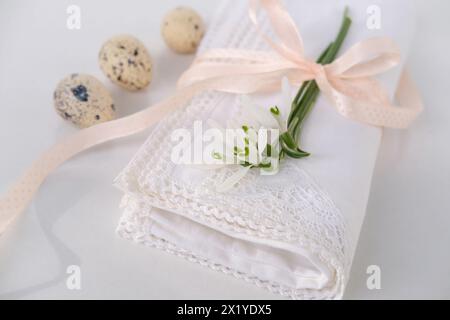 Weiße Leinenserviette mit handgefertigter Spitze, zarte Schneeglöckchenblume, drei Wachteleier liegen auf dem Lichttisch, luxuriöses Konzept für Frühlingsfrühstück Stockfoto