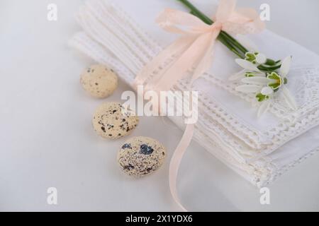 Weiße Leinenserviette mit handgefertigter Spitze, zarte Schneeglöckchenblume, drei Wachteleier liegen auf dem Lichttisch, luxuriöses Konzept für Frühlingsfrühstück Stockfoto